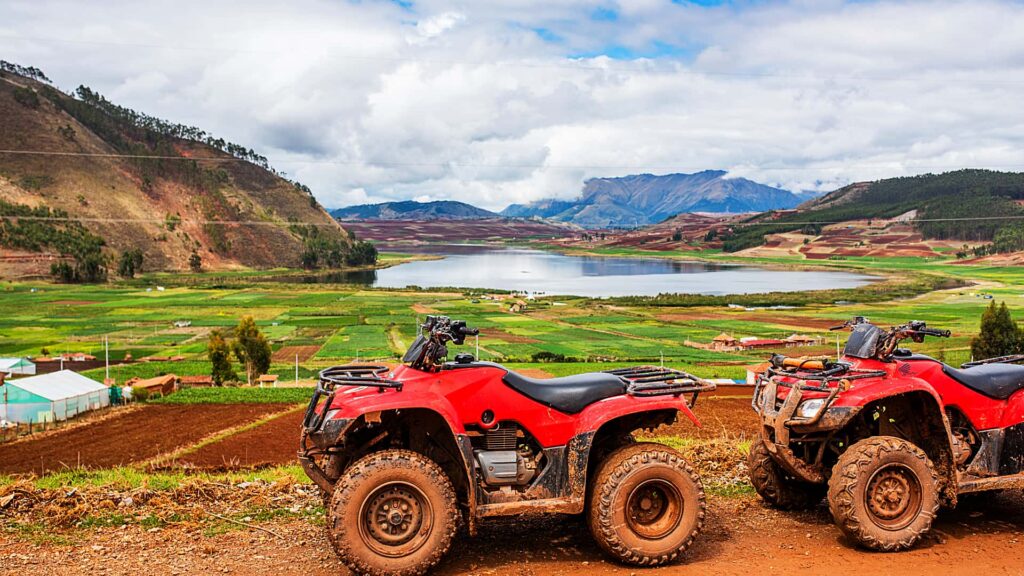 Turista en cuatrimoto roja frente a la laguna de Huaypo en el tour Maras Moray Cusco.
