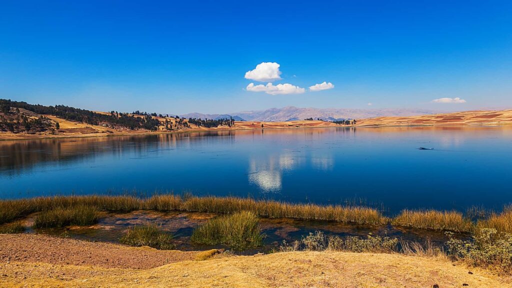Vista panorámica de la Laguna de Huaypo con reflejo del cielo azul durante el tour en cuatrimoto en Cusco.